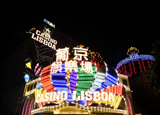 Bright neon signs in multiple colors illuminate the night, prominently displaying the name 'Casino Lisboa' alongside signage in Chinese characters. The lights form intricate patterns and vibrant displays, creating a lively and energetic atmosphere.